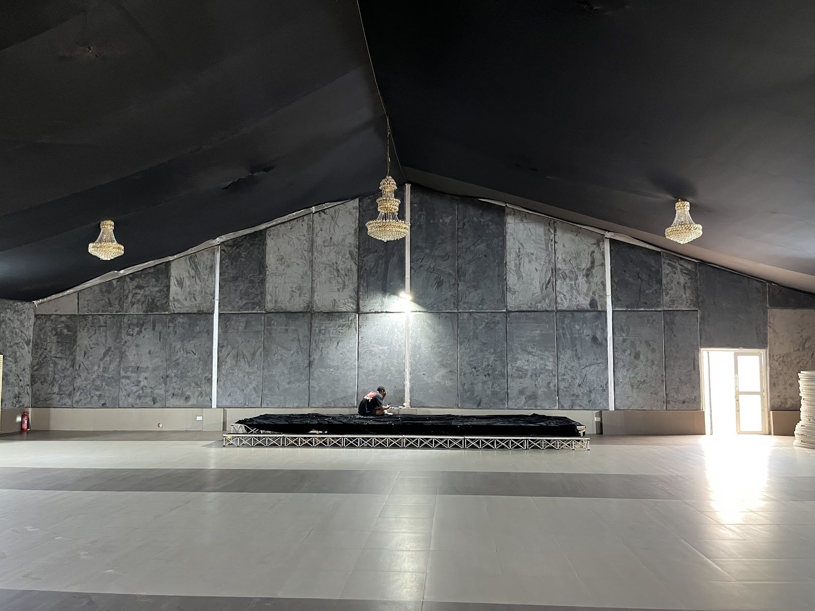 Empty hall with a black ceiling, chandeliers, a grey stone feature wall and a stage