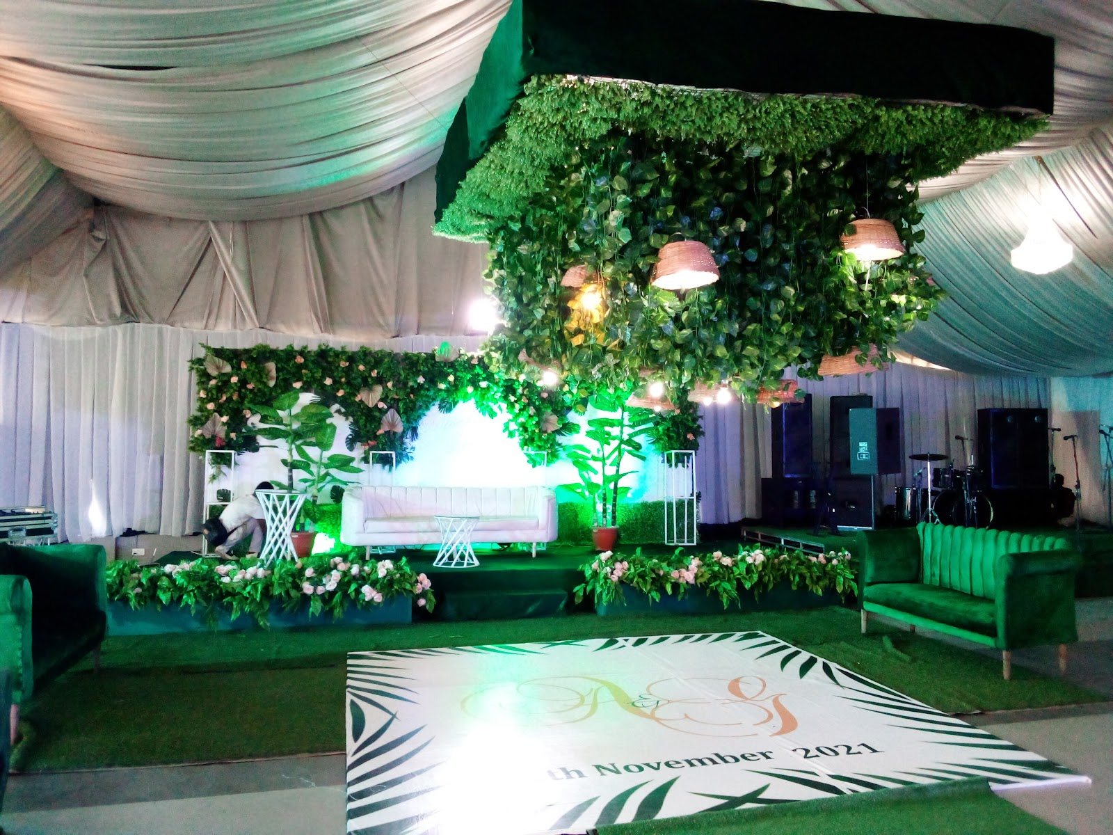 Green hedge feature and a lit dance floor with a printed monogram, under draped tent ceilings
