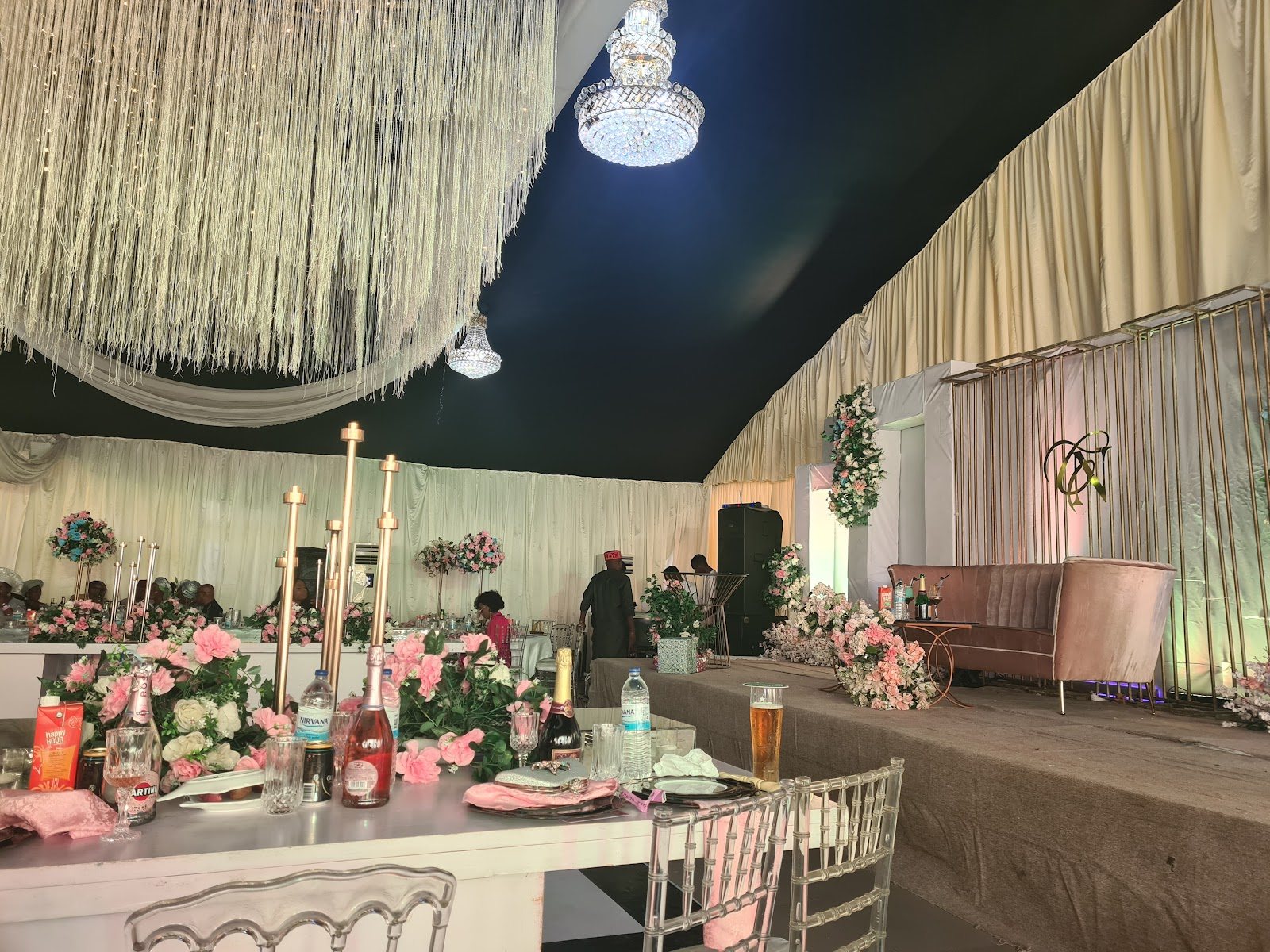 Stage with a sofa, pink florals and a ceiling hung with white strings, under a draped tent roof